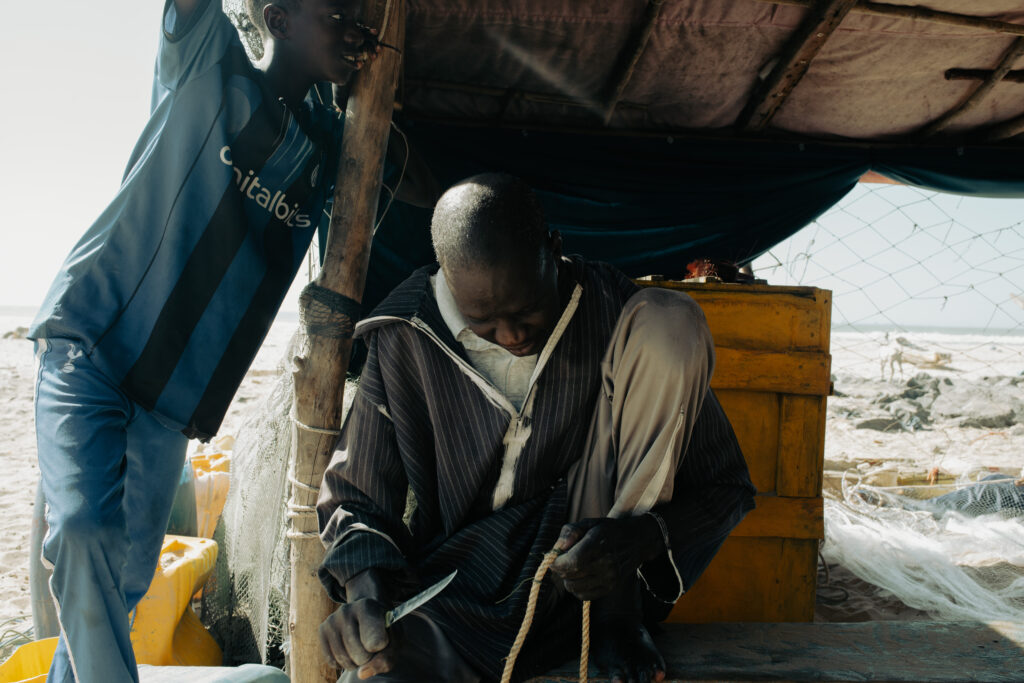 Pêcheur qui reprise un filet sous une case à palabre.